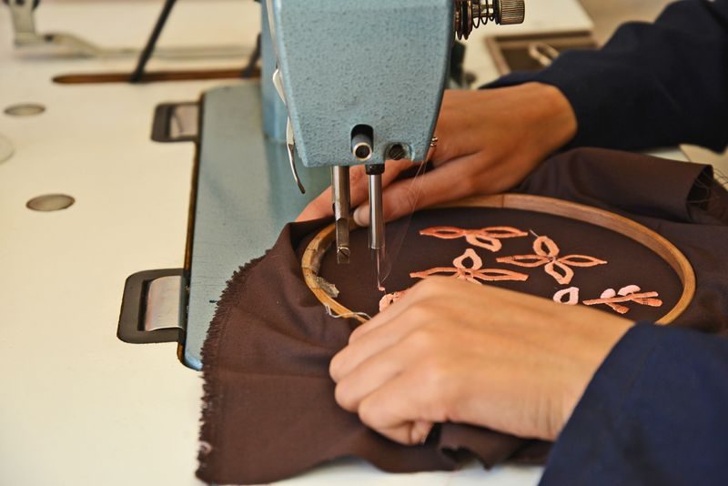 Hands guiding fabric in an embroidery hoop under the needle